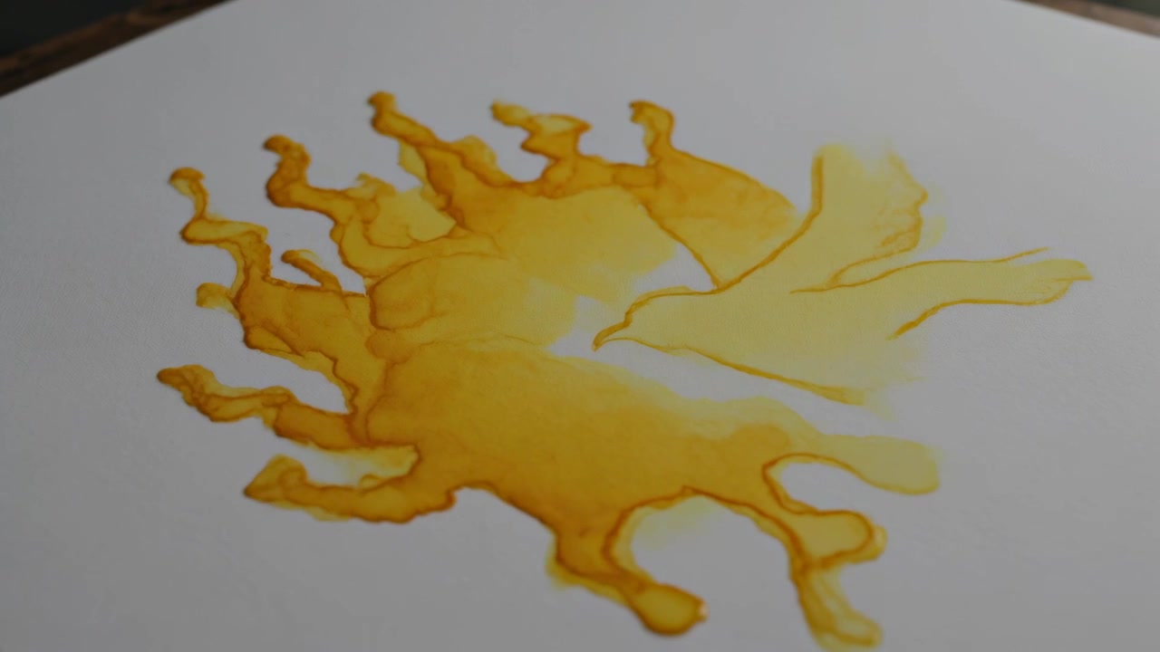 Gotas cayendo, una mancha amarillo-naranja extendiéndose sobre papel blanco en la mesa, formando un área con forma de pájaro.