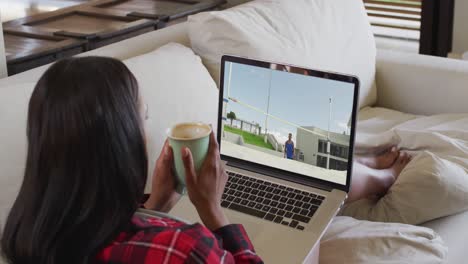 compuesto de una mujer sentada en casa sosteniendo un café viendo un evento de salto de altura en un portátil