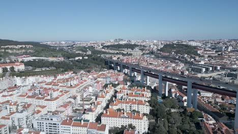 amazing aerial wide drone shoot of historic old town of lisbon, alfama in portugal with its buildings in amazing and varied pink blue and yellow colours with 25 april bridge on a calm sunny day