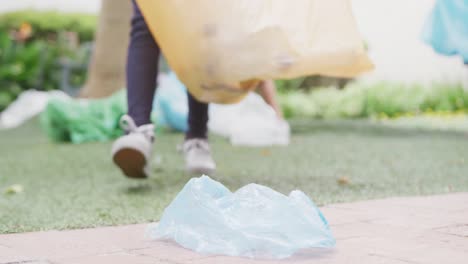 Video-of-low-section-of-biracial-schoolgirl-collecting-recycling-in-schoolyard,-copy-space