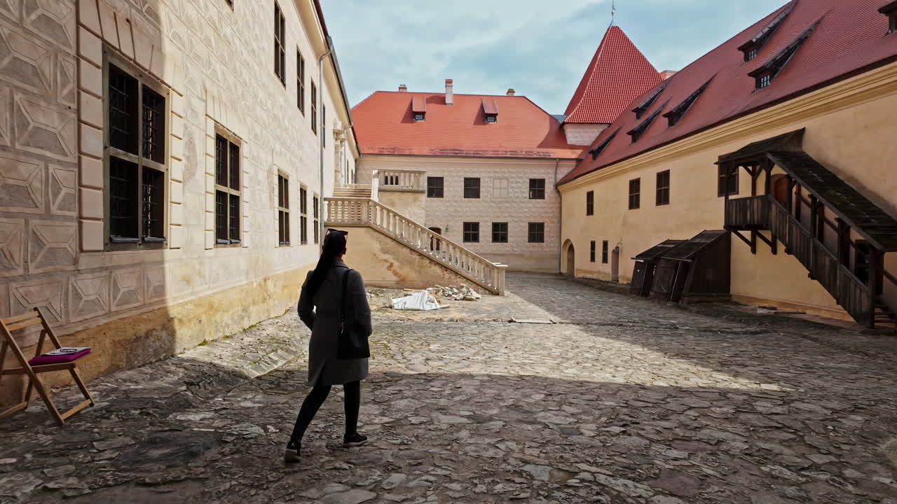 Žena prozkoumává nádvoří historického hradu Bauska za slunečného dne