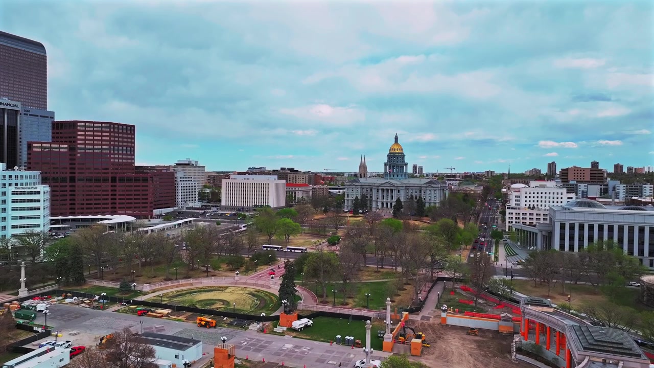 Paesaggio urbano aereo con drone del centro di Denver, che include il Civic Center Park, il centro eventi, Lodo, Capitol Hill e gli edifici del Campidoglio del Colorado, sotto un cielo blu nuvoloso primaverile, con auto e traffico che si muovono in avanti e verso l'alto nel pomeriggio.