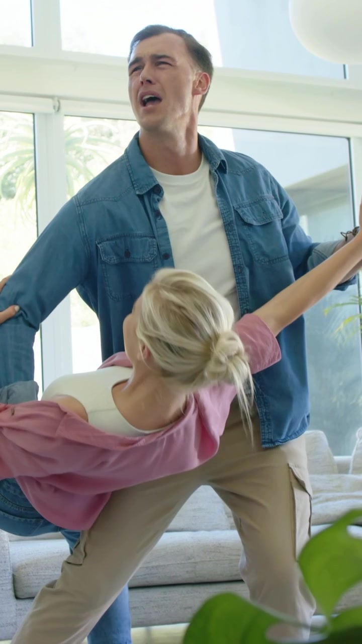 Vertical video: Reaching hand, man in denim guiding spins, supporting dip in living room with sofa
