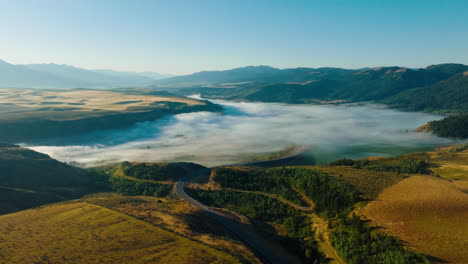 aerial view of a misty valley and winding road in a mountainous landscape at sunrise