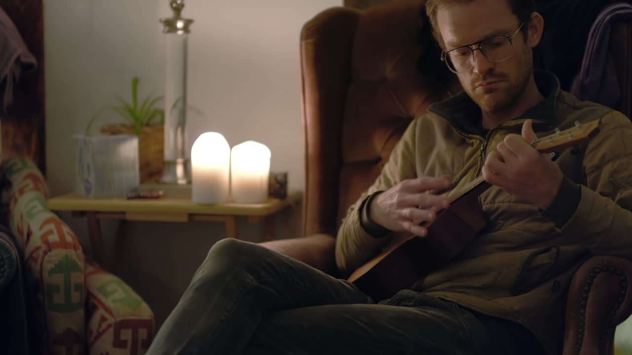 Gece bir koltukta oturan bir adam rahatlıyor ve ukulele çalıyor.