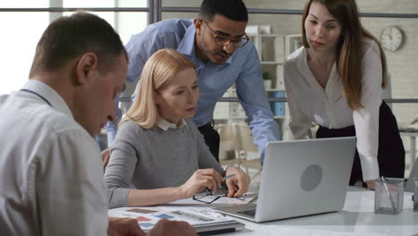 entrepreneur watching presentation on laptop and listening to young middle eastern colleague at office meeting