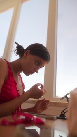 a woman making handmade crafts with beads by a window
