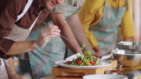 chef sirviendo ensalada en el plato con pinzas durante la clase culinaria