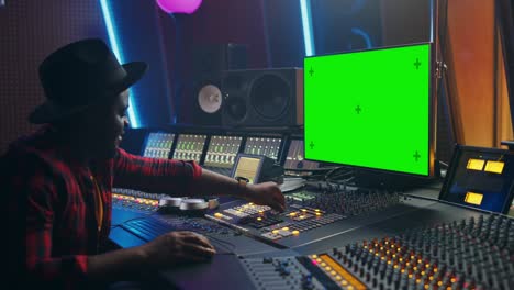 elegante ingeniero de audio productor que trabaja en un estudio de grabación de música, utiliza una computadora de pantalla verde, un ecualizador de placa de mezcla para crear nuevas canciones y canciones de éxito. músico artista negro creativo. retrato de vista lateral