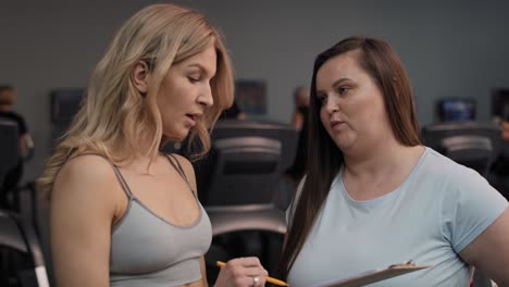 woman with overweight talking with female trainer in the gym.