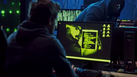 jóvenes hackers multiétnicos, hombres y mujeres sentados en la habitación oscura por la noche en las computadoras mientras trabajan con programas de software