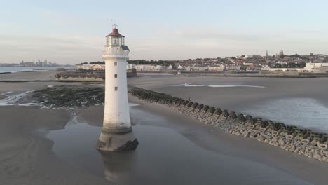 Aerial-pull-back-orbit-right-view-across-British-Lighthouse-and-coastal-seaside-town-beach-breakers