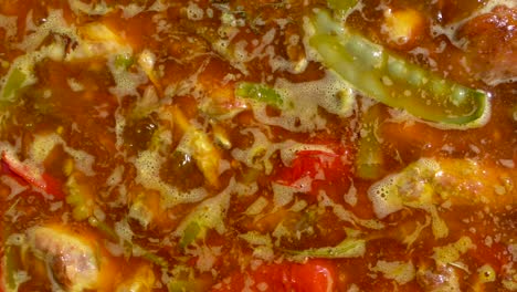vista de arriba hacia abajo de un guiso hirviendo con verduras y carne que pronto se convertirá en una paella española, en cámara lenta de izquierda a derecha.