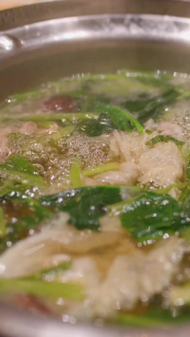 Primo piano di una tradizionale zuppa hotpot che bolle, mostrando carne fresca, verdure a foglia, funghi e brodo
