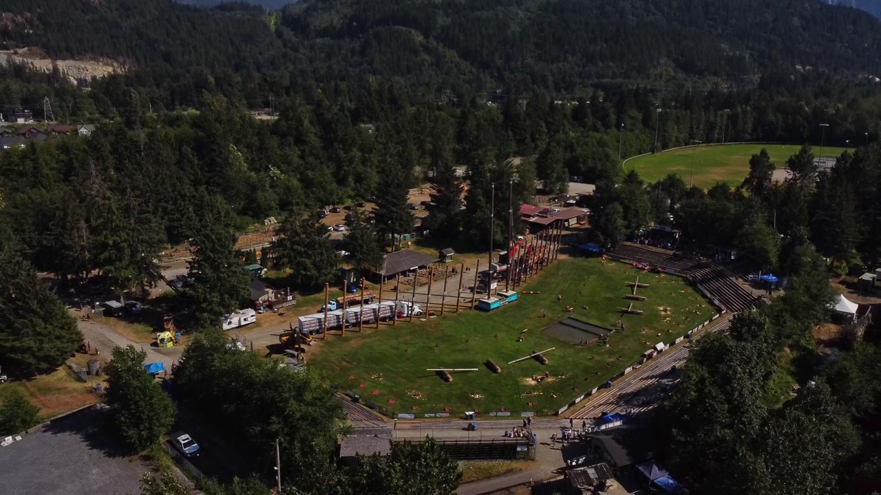 Una vista aerea mozzafiato di una natura selvaggia montuosa a Squamish, BC, Canada. Cielo blu con foreste e campi d'erba che circondano uno stadio competitivo per festival e concerti durante tutto l'anno