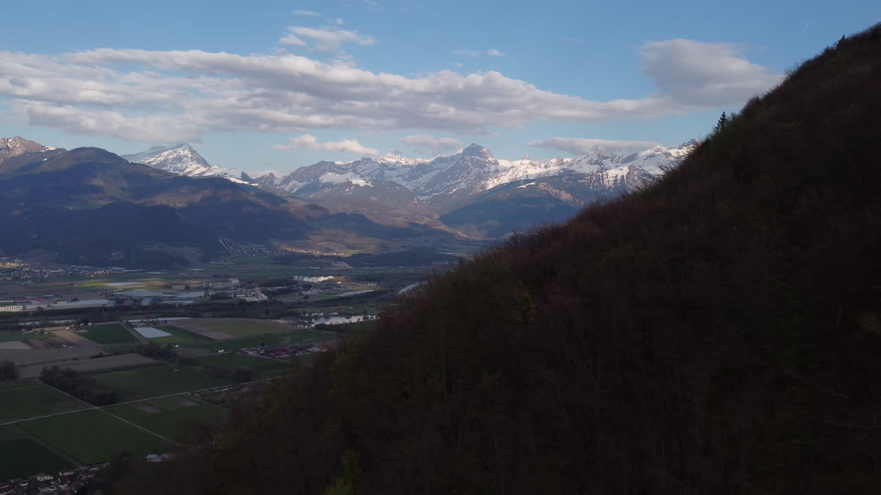 Slow expansive aerial shot next to the mountains of Vionnaz, Switzerland with the Alps in the background.
