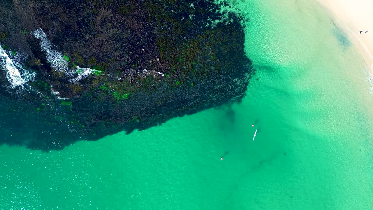 Drone aerial landscape of kayaker paddling out of beach bay channel inlet with rocky reef coastline swell along ocean headland in rural town Norah Head Central Coast Australia tourism travel leisure
