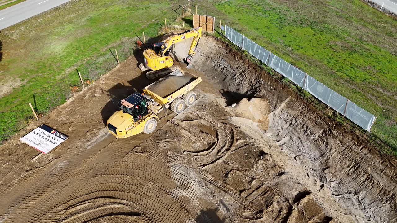 Drone footage captures an excavator and dump truck at a construction site in Cromwell, New Zealand, highlighting earthmoving activities