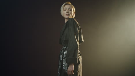 camera moving from feet to up of the stylish caucasian woman standing on the black background with single lamp light and having photosession