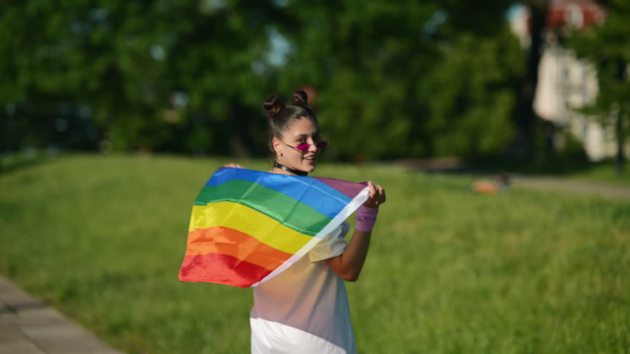 mujer sosteniendo una bandera arco iris en un parque