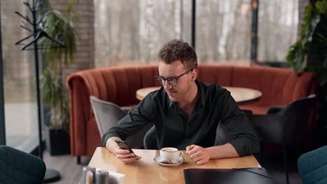 cute curly man in a cafe spends time on a smartphone