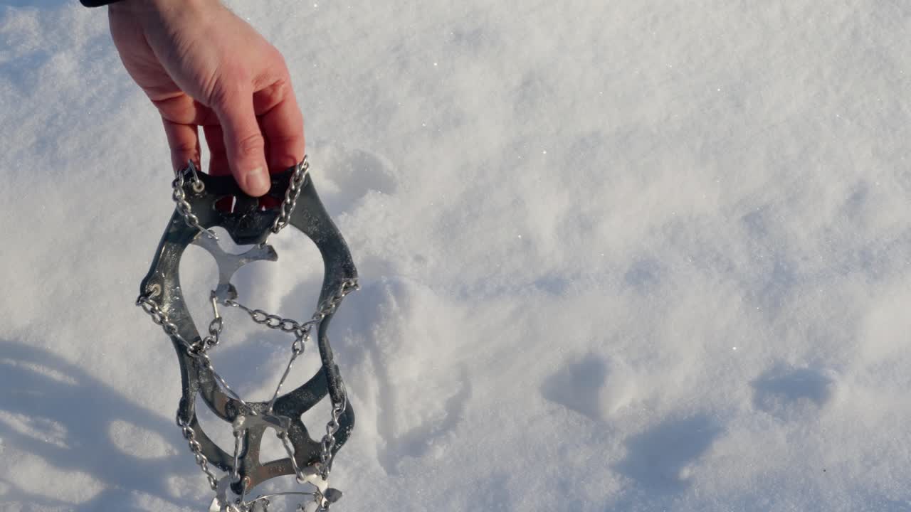 Person carefully places pair of ice cleats on fresh snow, high angle, close up.