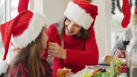 madre caucásica feliz limpiando la boca de su hija en la mesa de navidad