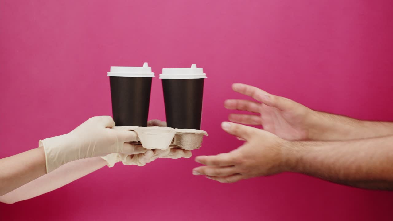 Mano guantata che consegna tazze di caffè da asporto su sfondo rosa