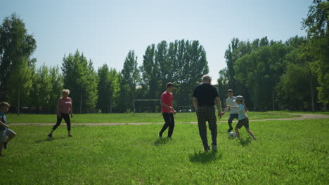 siblings and their grandfather enjoy a sunny day playing football together in a lush green field