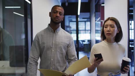 Asian-businesswoman-walking-using-smartphone-going-through-paperwork-in-modern-office