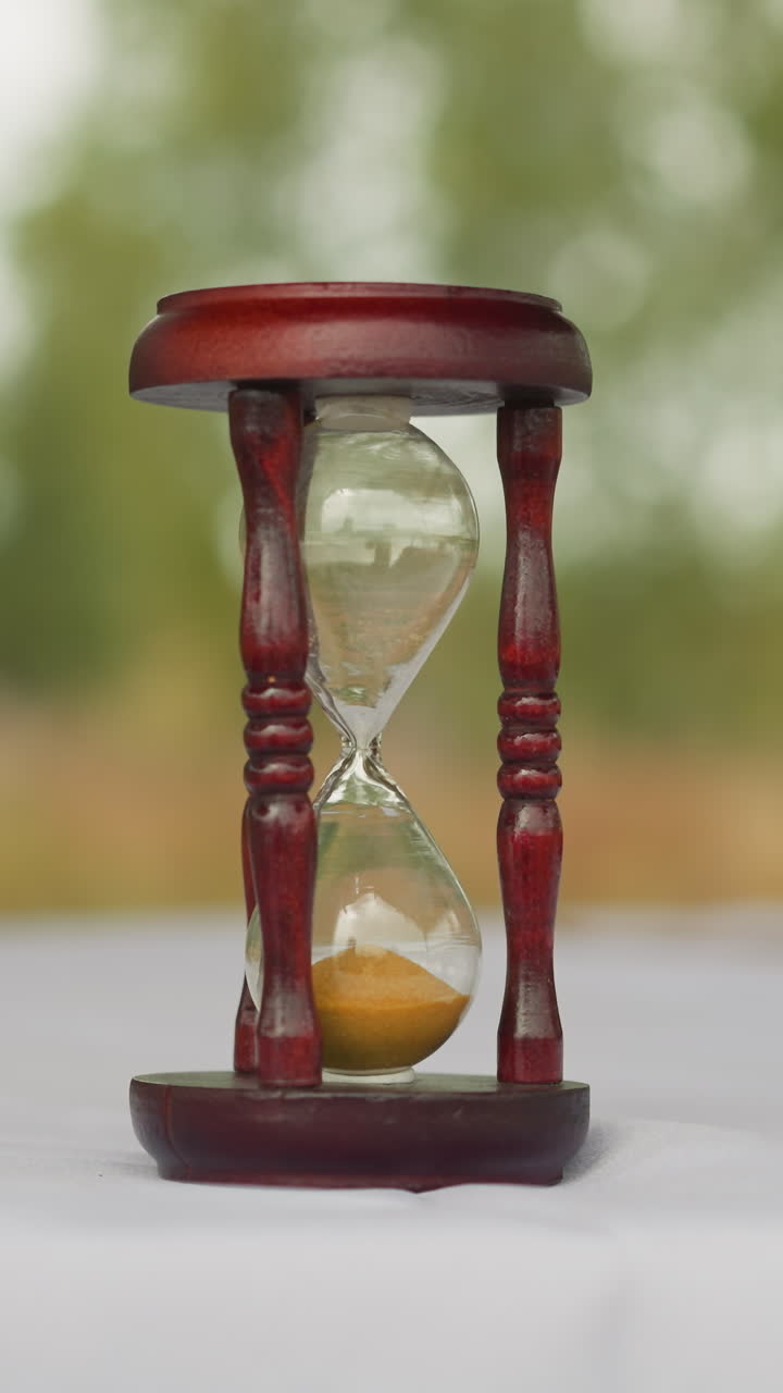 Hourglasses stand on table in yard. Ancient device for measuring passage of time. Glass bulbs with sand connected by narrow neck on blurred background