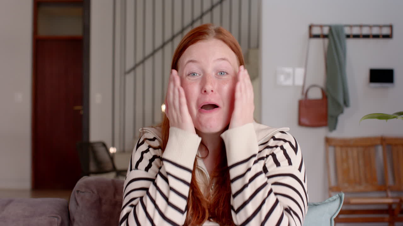 Smiling woman with red hair sitting on couch, talking on video call