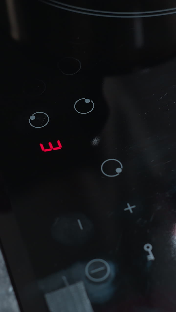 primer plano de la mano del cocinero ajustando los ajustes de temperatura en la estufa eléctrica moderna, el panel de control táctil refleja la mano del cociner y la cocina circundante mientras preparan una comida