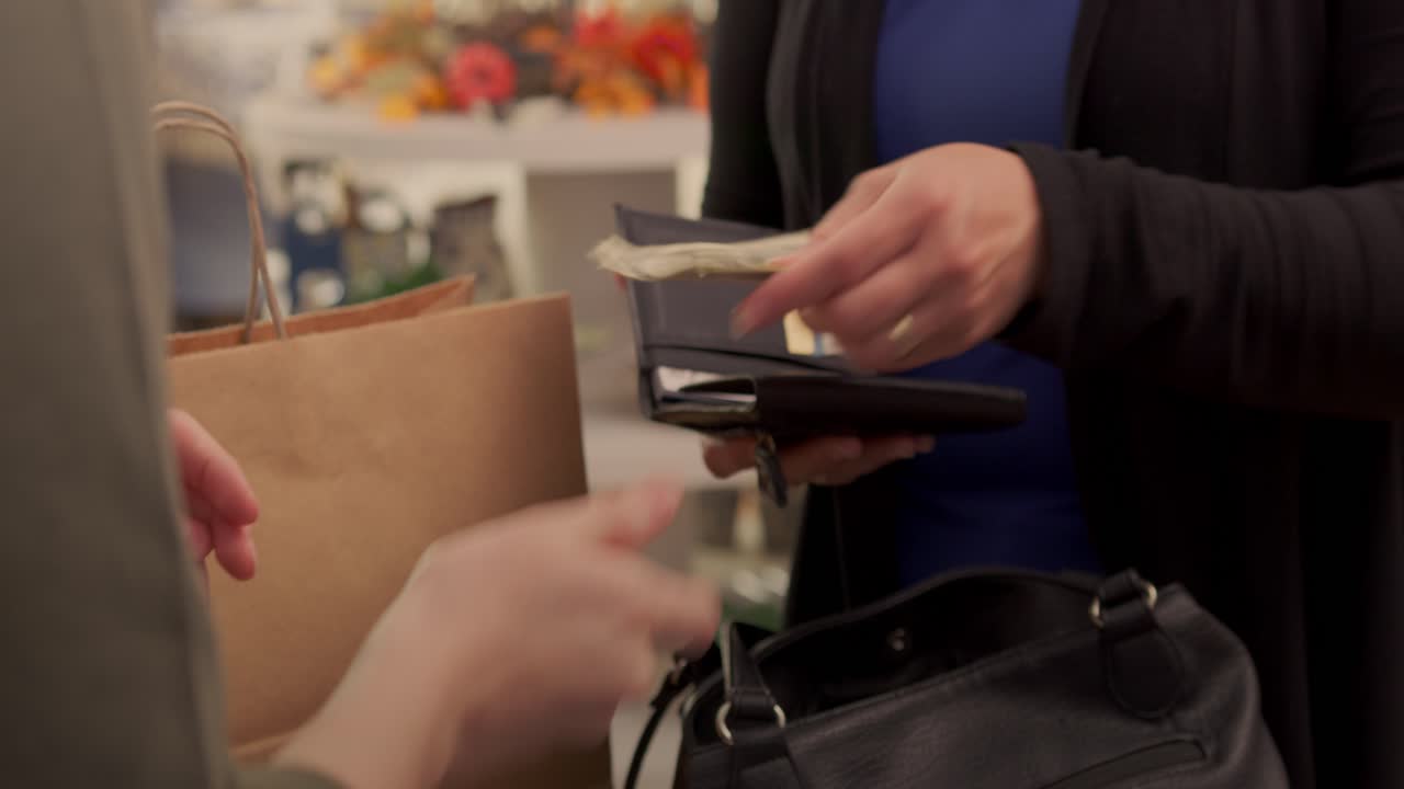 Cassiere di minimarket vende un articolo a un cliente in un sacchetto marrone, consegnando il resto dal portafoglio in una luminosa e calda giornata autunnale