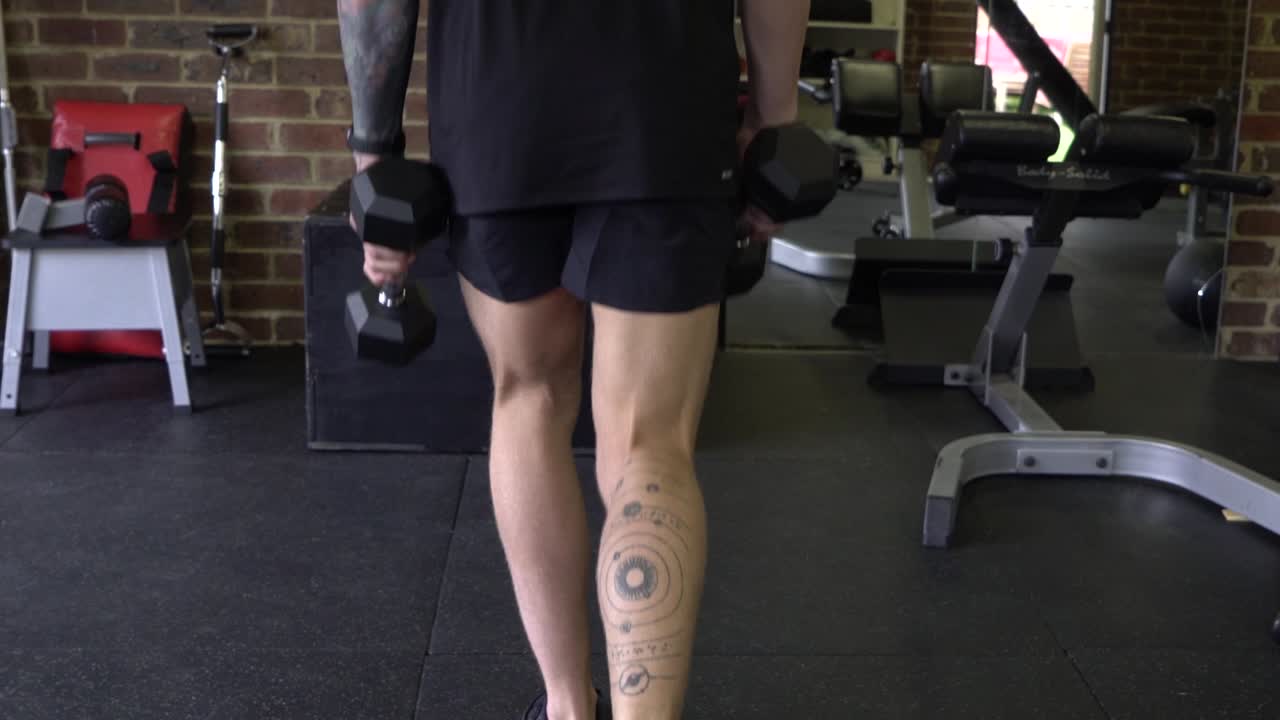 아령 리버스 런지 정적 운동을 하는 홈 체육관에서 근육질의 남자