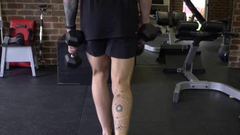 hombre musculoso en el gimnasio en casa haciendo ejercicio con pesas estocadas inversas estáticas