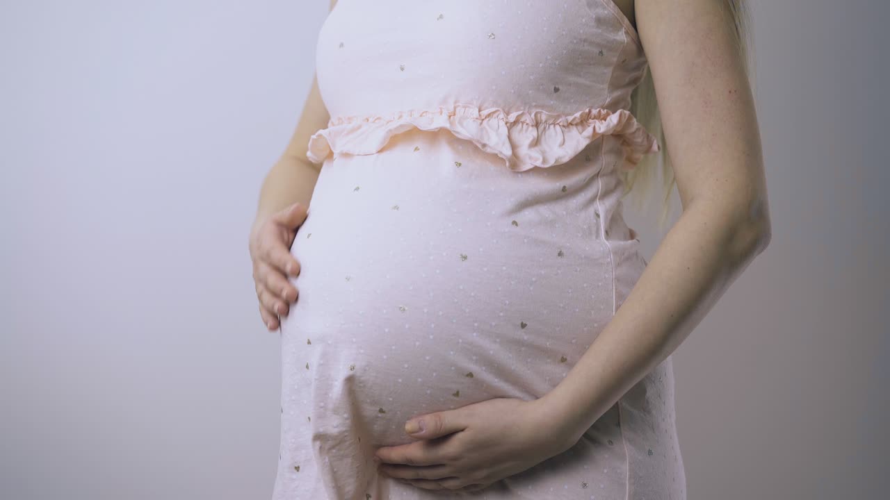 mujer esperando a un bebé acaricia el abdomen en un primer plano de la habitación de luz