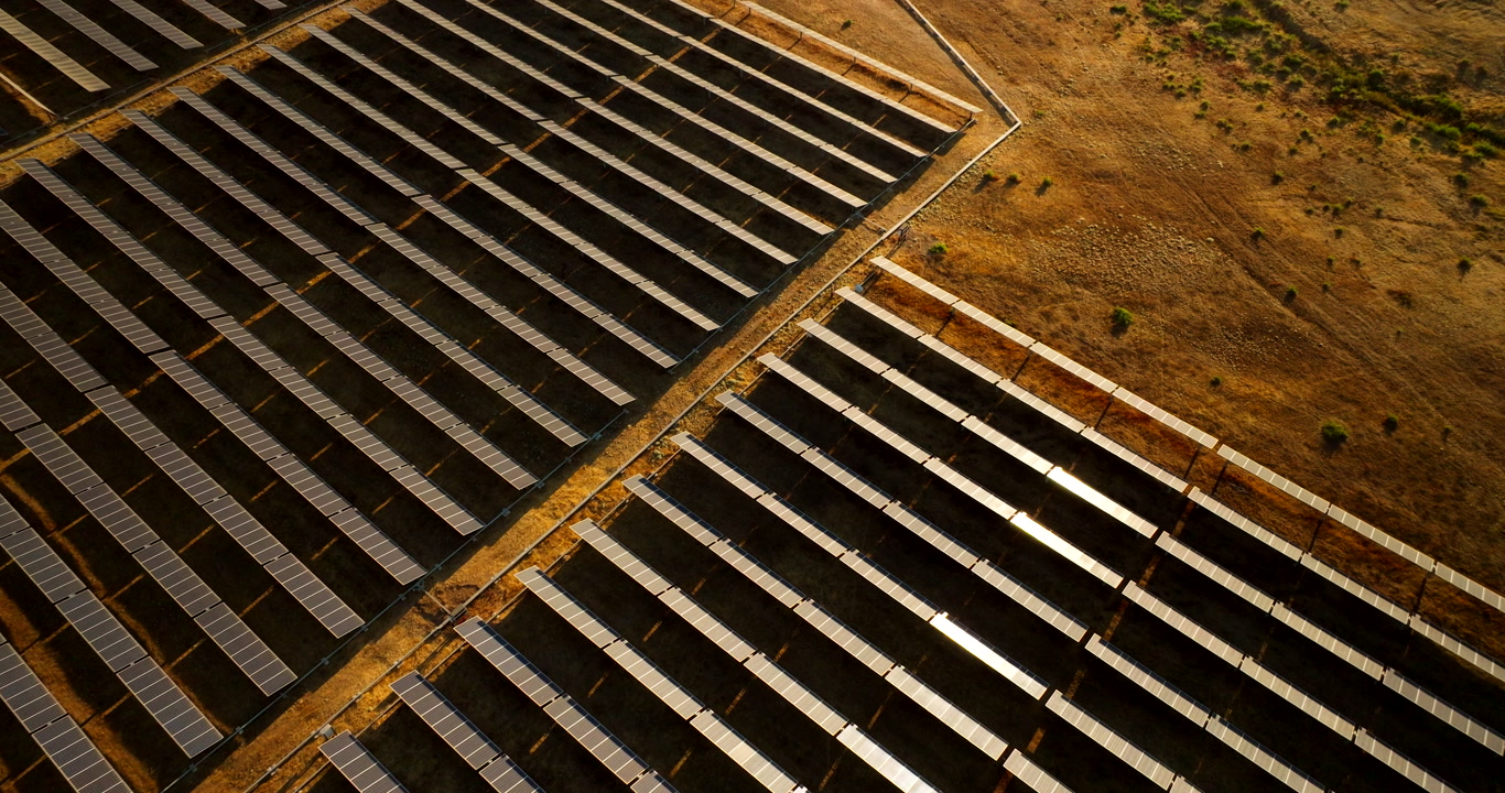 Neat rows of PV panels on South American solar park, sunset aerial tilt-up