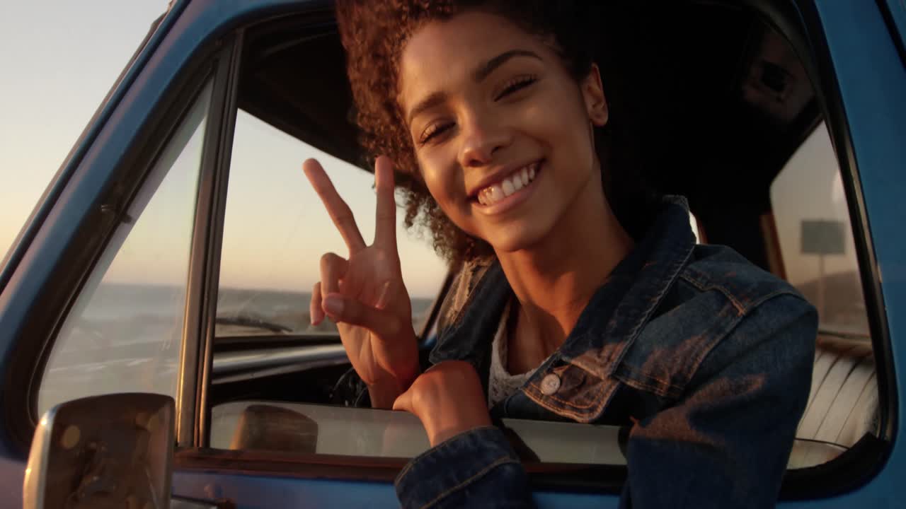 mujer mostrando un signo de victoria en una camioneta en la playa 4k