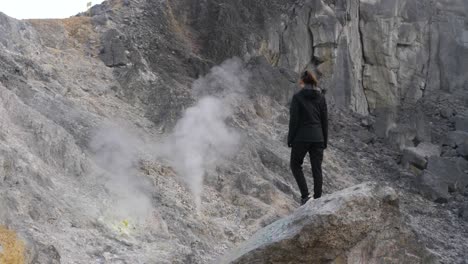 Toma-En-Cámara-Lenta-De-Una-Mujer-Parada-En-Una-Roca-Mirando-El-Humo-De-Azufre-Del-Volcán-En-El-Norte-De-Sumatra,-Indonesia