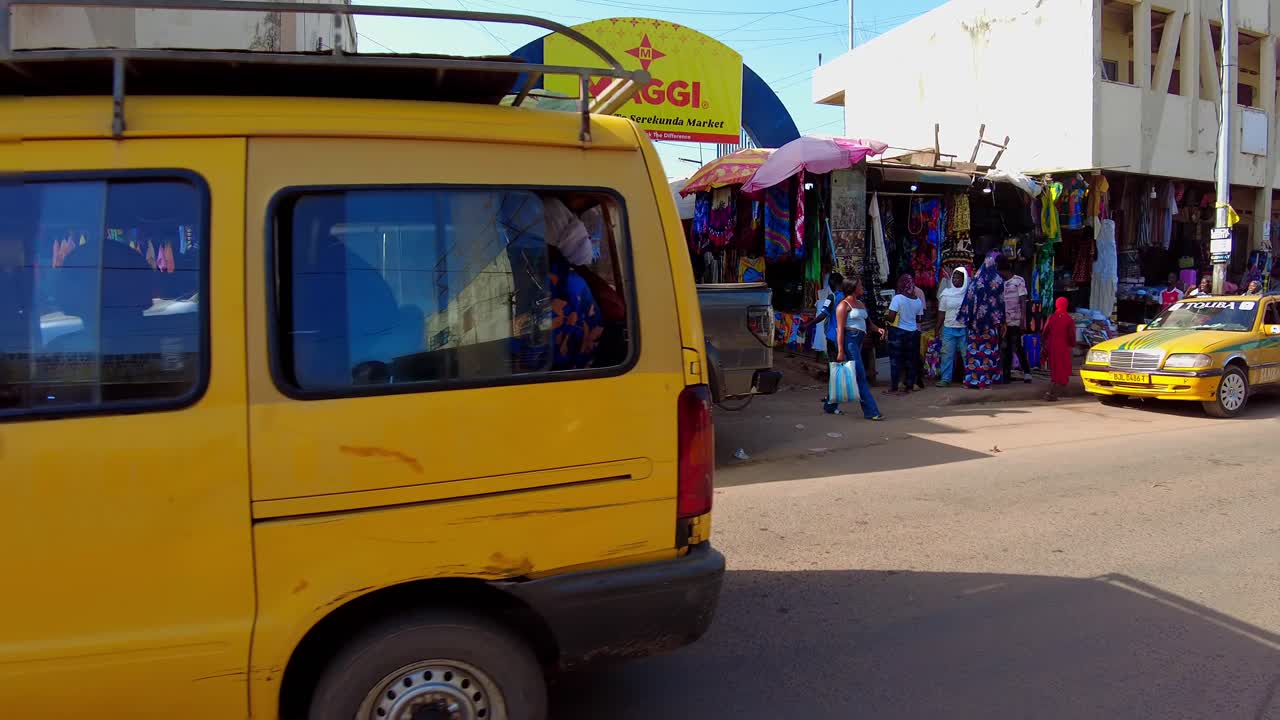 POV walking through Serekunda Market Entrance from main street during sunny summer day