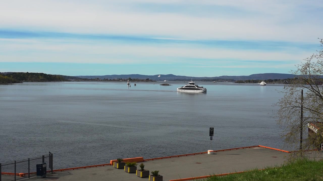 Håndholdt vidvinkelbilde fanger en luksuriøs yacht som glir over Oslofjorden, sett fra Operataket. Rolig vann, fjerne åser og mykt dagslys skaper en fredelig skandinavisk scene