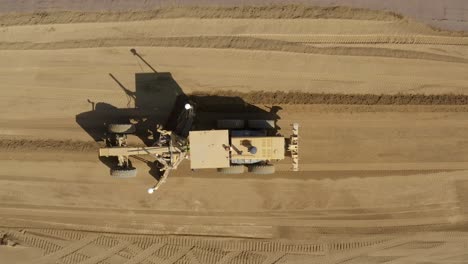 Top-down-Aerial-view-of-a-road-grader-pushing-and-leveling-dirt-on-a-construction-site