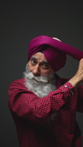 vertical video low key studio lighting shot of senior sikh man with beard tying fabric for turban against dark background 4