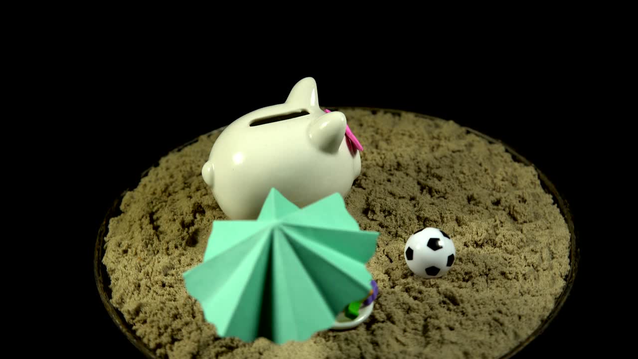 una alcancía blanca se encuentra en una playa de arena y gira sobre un fondo negro.