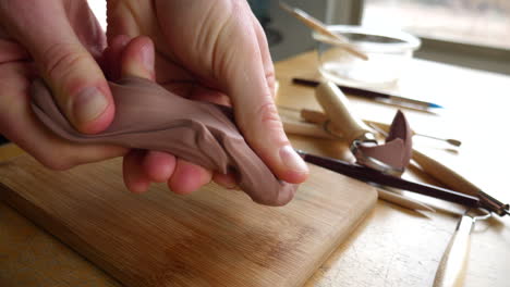 slide across the hands of an artist sculpting with brown modeling clay on a wooden table with tools strewn about the art studio