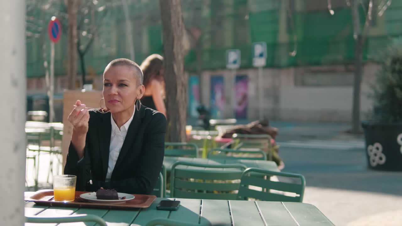 Bald Woman Enjoying Cake and Orange Juice at Outdoor Cafe