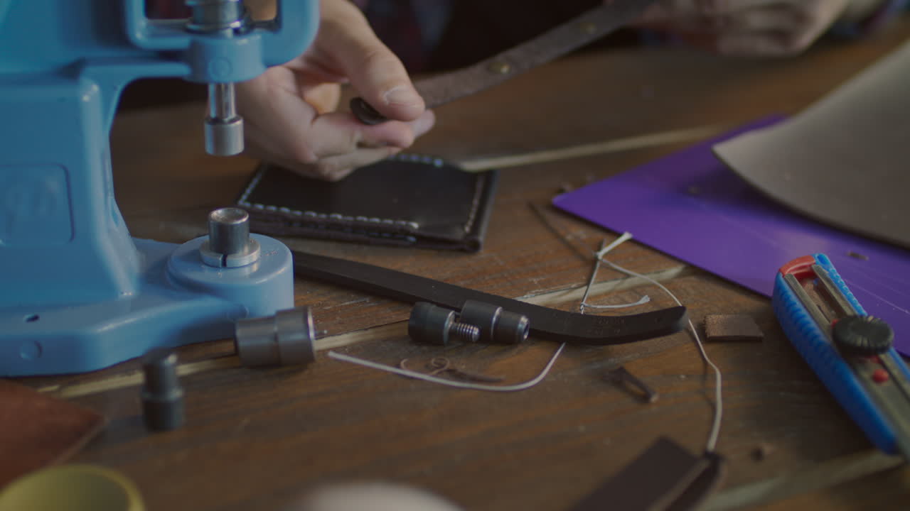 trabajador inserta botón de metal en el cinturón. fabricación de accesorios de cuero