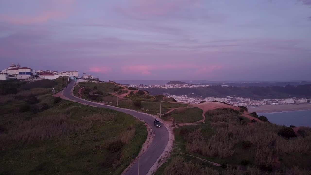 автомобиль едет по извилистой дороге рядом с обрывом с красивым городским пейзажем на заднем плане