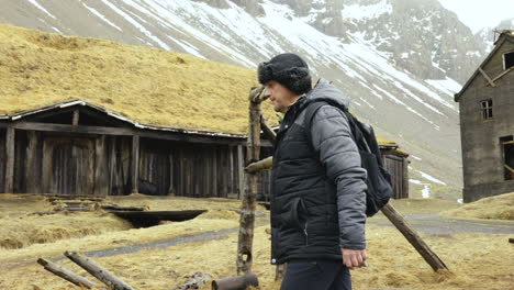 middle age man walking in warm clothes by replicas of viking village buildings in landscape of iceland